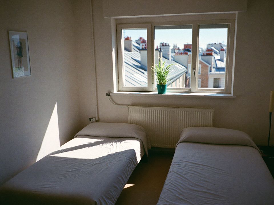 Bright twin room with two made beds and a window onto city roofs